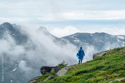 man in a blue raincoat on the edge of a cliff looks into the distance