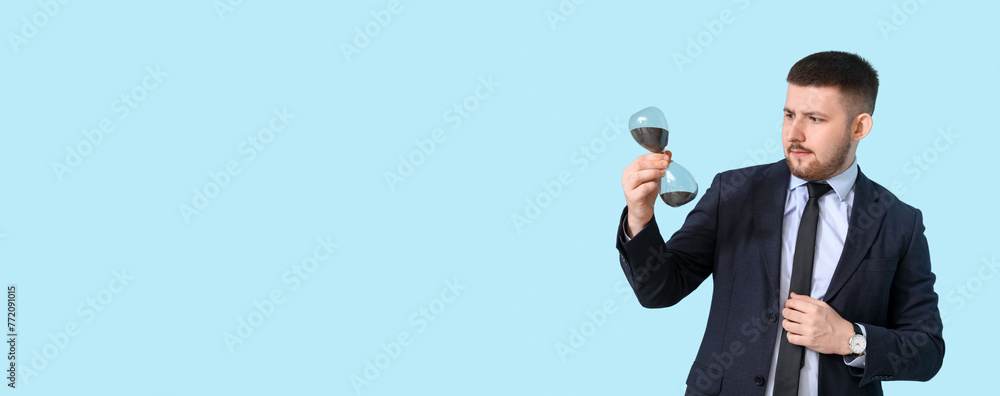 Young thoughtful businessman with hourglass on blue background. Time management concept Young thoughtful businessman with hourglass on blue background. Time management concept