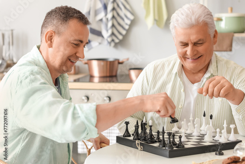 Mature brothers playing chess at table in kitchen