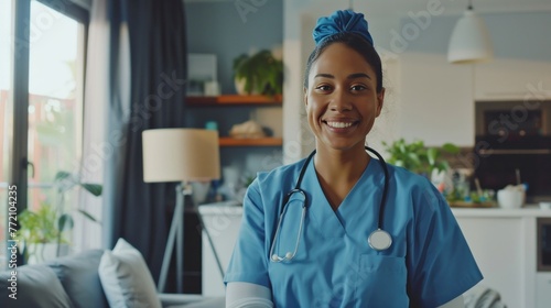 A smiling healthcare professional in blue scrubs with a stethoscope, standing in a cozy, well-lit home interior. photo