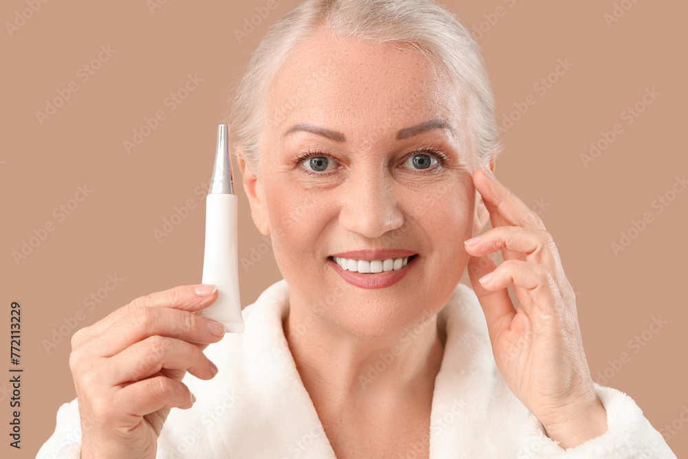 Beautiful mature woman with eye cream on brown background, closeup Beautiful mature woman with eye cream on brown background, closeup