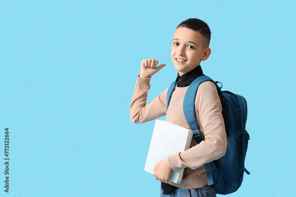 Fototapeta premium Cute schoolboy with book and backpack on blue background
