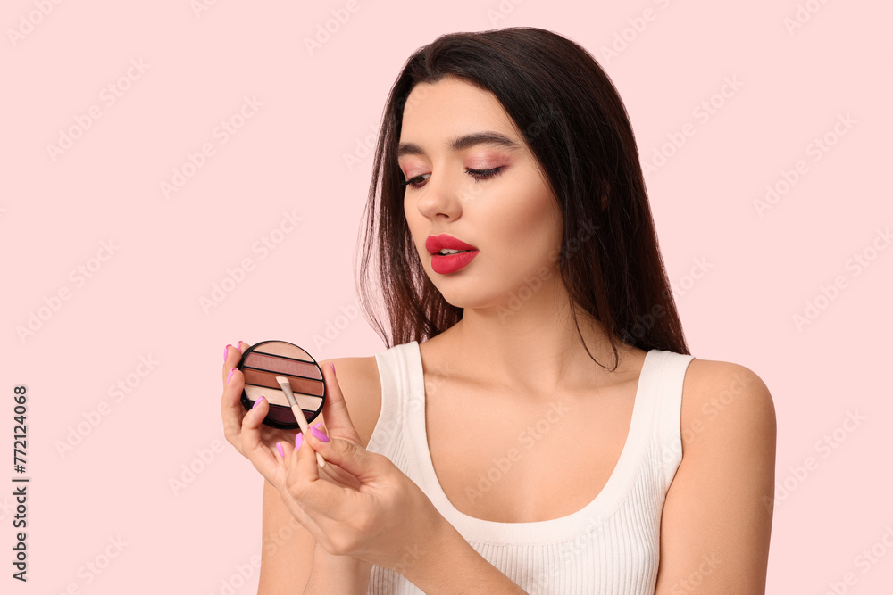 Beautiful young woman with eyeshadows and brush on pink background Beautiful young woman with eyeshadows and brush on pink background