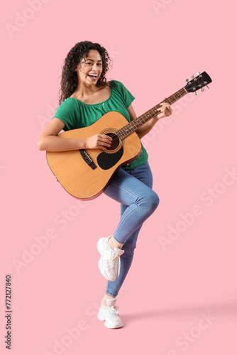 Young African-American woman playing acoustic guitar on pink background