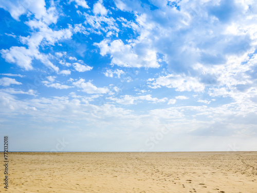 The background texture of a vast expanse of beach sands, with visitors' footprints, and clouds scattered in a pattern on sky. Concept of a peaceful, breezy day at the seaside. Copy space for design.