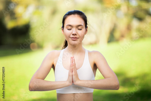 Tranquil young woman with eyes closed in Namaste pose, practicing mindful meditation in a bright