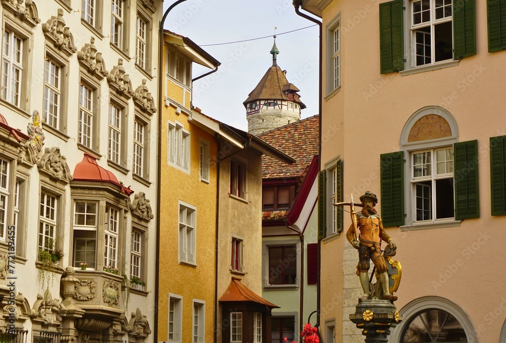 European street with ornate buildings, tower in the background and statue in foregrownd