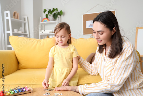 Female psychologist with little girl doing puzzle in office