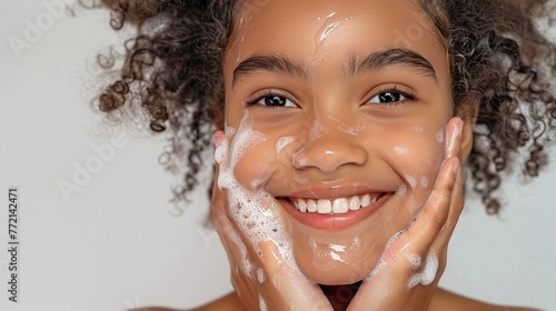 A smiling African American girl with curly hair and soap suds on her face on a grey background