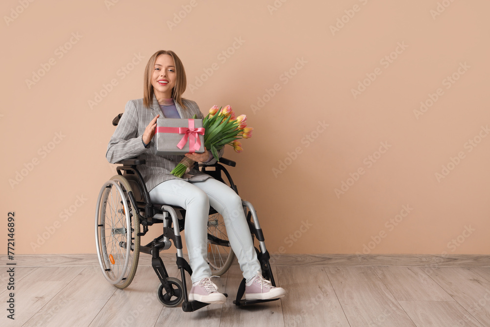 Young woman in wheelchair with tulips and gift near beige wall. International Women's Day Young woman in wheelchair with tulips and gift near beige wall. International Women's Day