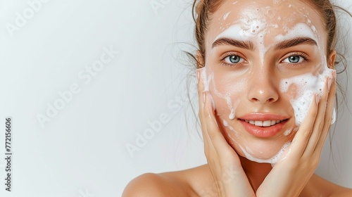 Photo of a smiling white woman with clear skin washing her face with soap on a grey background