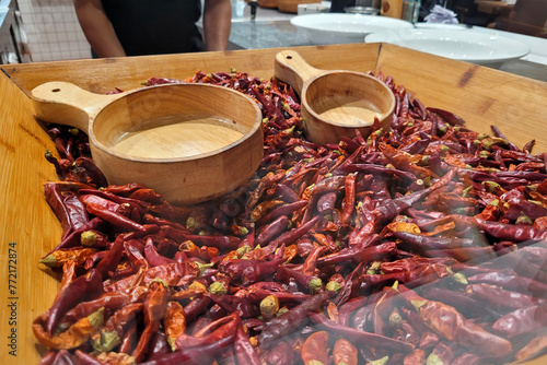 A wooden tray in a restaurant holding a heap of Chinese dry chili and Sichuan peppercorns.