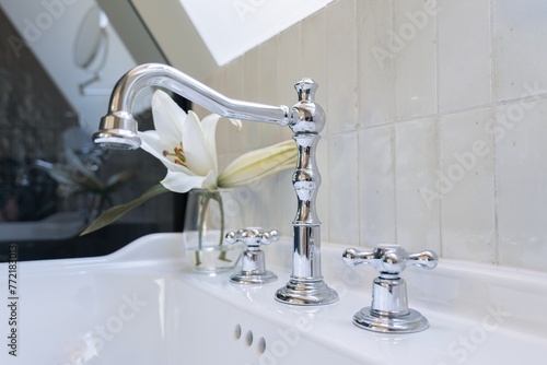 Bathroom sink with a faucet, vase of flowers, and glass vase on metal counter