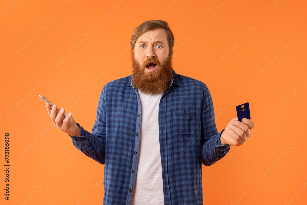 Shocked Unhappy Man Holding Smartphone And Credit Card In Studio Shocked Unhappy Man Holding Smartphone And Credit Card In Studio