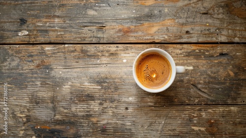 Top view of a freshly brewed espresso in a white cup on a rustic, worn wooden table, showcasing rich textures and coffee's robust essence. photo