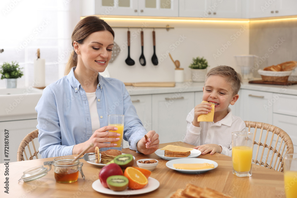 Mother and her cute little son having breakfast at table in kitchen