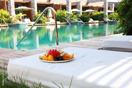 Cuadro en lienzo Plate with fresh fruits on sun lounger near outdoor swimming pool