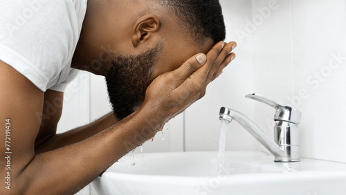 Man rinsing face with water in bathroom sink