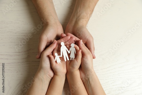 Parents and child holding paper cutout of family at white wooden table, top view