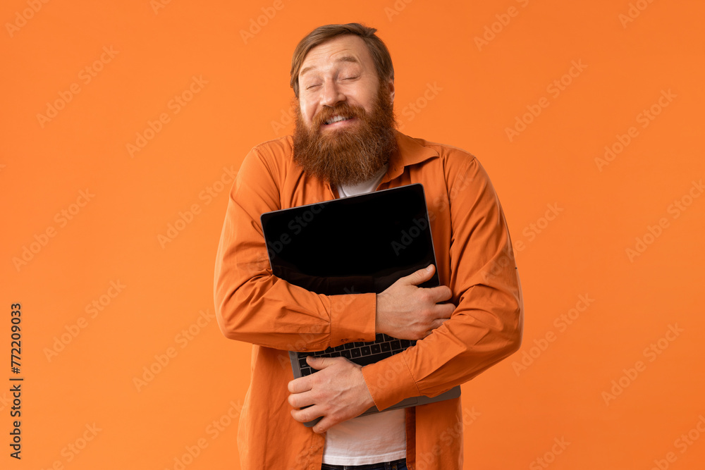 Happy Redhaired Bearded Man Hugging His Laptop Computer, Orange Studio Happy Redhaired Bearded Man Hugging His Laptop Computer, Orange Studio