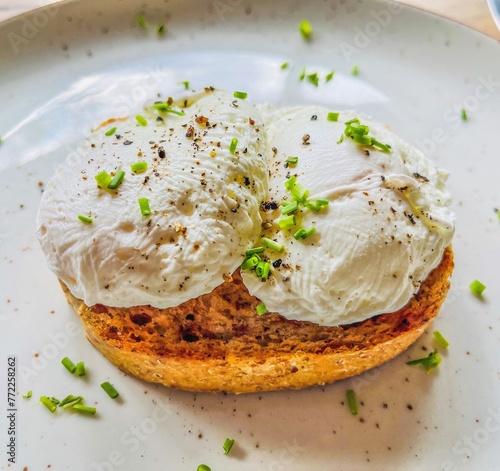 Two poached eggs on brown toast, plated on a white background with chopped chives
