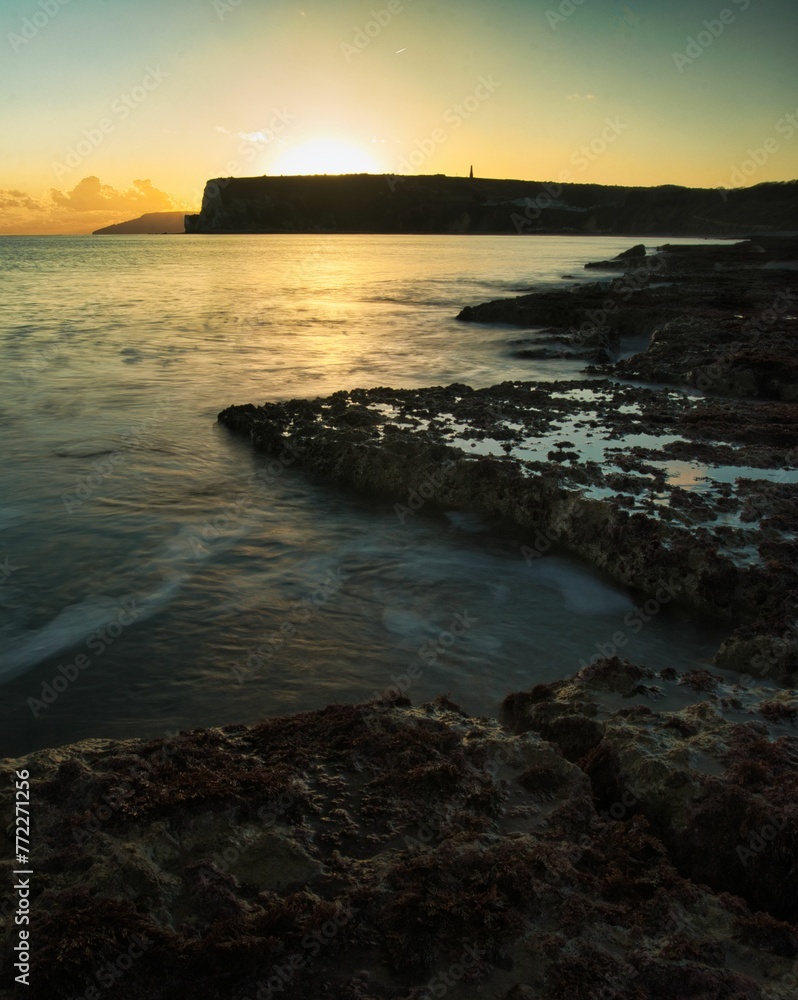 Breathtaking shot of a tranquil ocean at sunset, with a stunning array of rocks in the foreground Breathtaking shot of a tranquil ocean at sunset, with a stunning array of rocks in the foreground