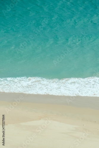 Vertical shot of a sandy beach coastline, with soft, rolling waves of the ocean lapping onto shore