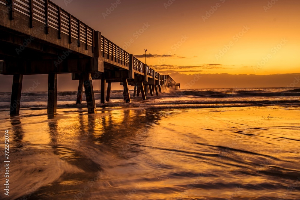Wooden pier jutting out into a pristine beach, with a sunset illuminating the horizon Wooden pier jutting out into a pristine beach, with a sunset illuminating the horizon
