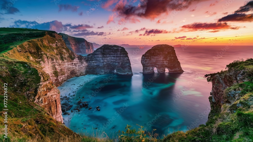 Beautiful beach with high cliffs and a blue sea at sunset. The sky is orange and pink. The cliffs are brown and grey, and there are two large rocks in the sea, which appear grey. Beautiful beach with high cliffs and a blue sea at sunset. The sky is orange and pink. The cliffs are brown and grey, and there are two large rocks in the sea, which appear grey.