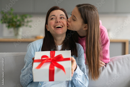 Mother's day, teen daughter give gift box to mum and kissing her on cheek, sitting on sofa, woman happy smiling, enjoy family time