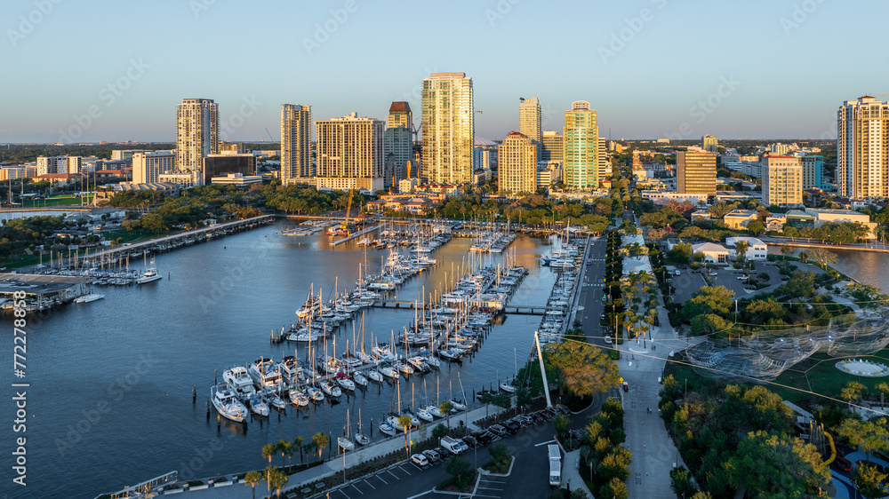 Fototapeta premium Golden sunrise illuminates downtown Saint Petersburg, Florida, highlighting boats at the yacht club, waterfront park, and cityscape.