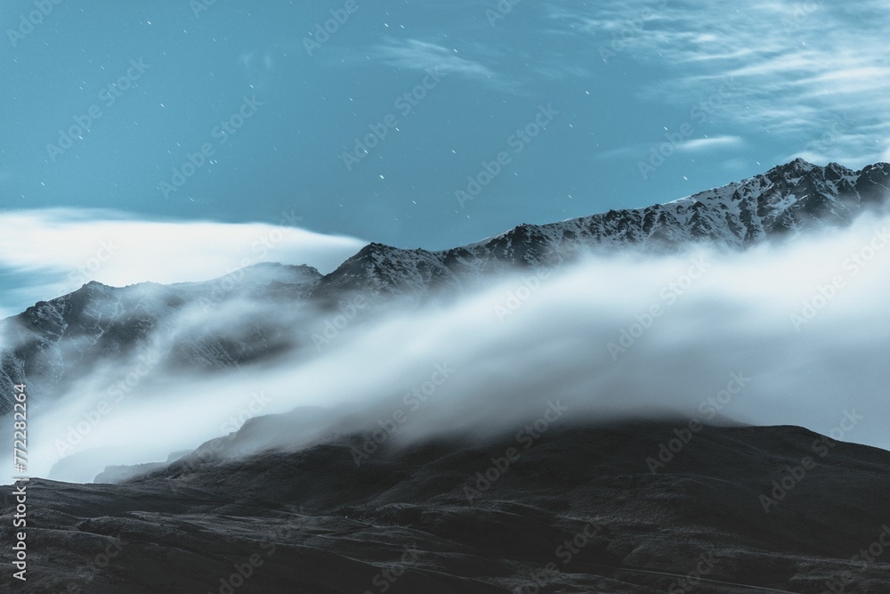 Obraz premium Picturesque winter landscape featuring a snow-capped mountain surrounded by fluffy clouds