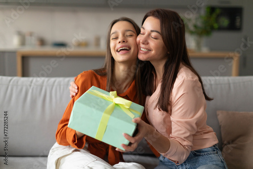 Happy mother congratulating her loving daughter with birthday at home, give her gift box and embrace. Family holidays