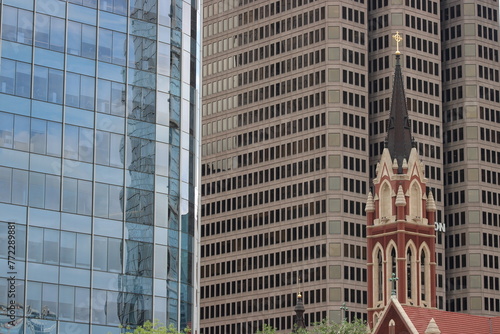 City skyscrapers overshadow the steeple and bell tower of a Spanish Cathedral on a city street. 