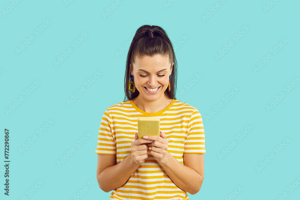 Happy woman looking at screen of her mobile phone and smiling. Studio shot of cheerful beautiful young lady using modern cellphone, text messaging, communicating on social media and having good time Happy woman looking at screen of her mobile phone and smiling. Studio shot of cheerful beautiful young lady using modern cellphone, text messaging, communicating on social media and having good time