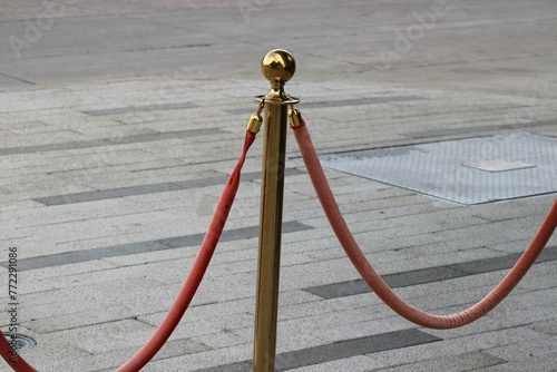 A sidewalk red velvet rope attached to a gold plated standard for lines forming for patio seating.