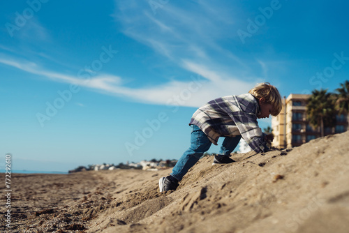 The boy jumps up on the sandy beach near the sea. a 3-year-old boy in a checkered shirt plays on the sand. cheerful active baby jumping on the sand