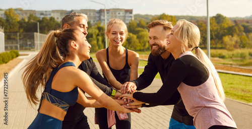Happy smiling sporty group of people standing in a circle with hands in stack in the morning after sport training in the city park. Workout in nature and healthy lifestyle concept. Banner.