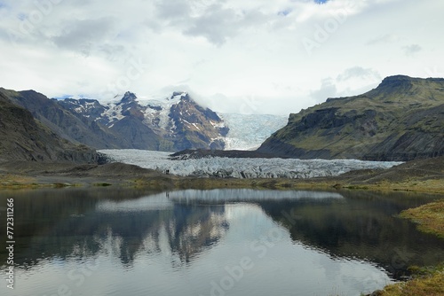 Tranquil lake in a lush meadow surrounded by snow-capped mountains and a glacier in the distance