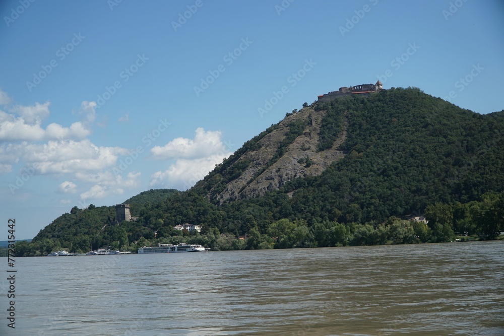 Majestic mountain surrounded by lush trees along the banks of a tranquil river in Visegrad, Hungary