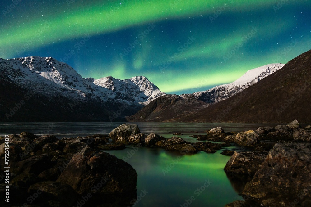 Night sky featuring spectacular aurora borealis lighting up the snow-capped mountains.