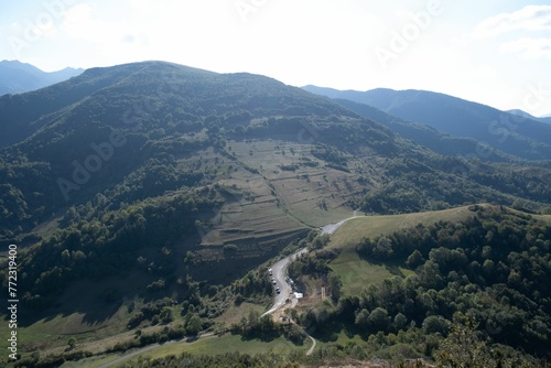 Scenic landscape of a green mountainous terrain featuring lush green trees, against the bright sky