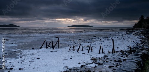 an ice covered beach on the water with dark clouds in the background photo