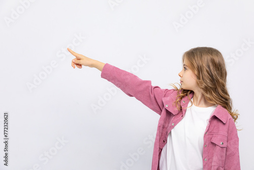 Calm girl stands sideways, looks into the distance, points with her index finger at something isolated on a white background. Copy space. Mock up. place for your advertising