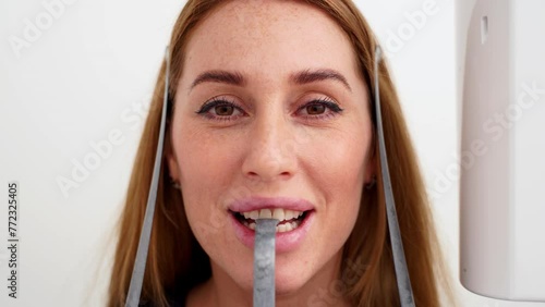 Close-up of woman's face with head positioned in cephalometric panorama x-ray machine. Female patient standing in dental x-ray machine for dental radiography. Woman making panoramic shot of jaw. photo