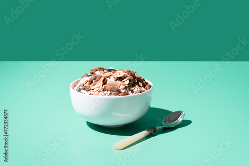 Cereal de granola muesli en un tazón blanco con cuchara sobre fondo verde	