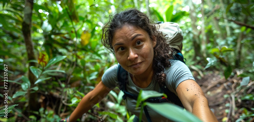 A determined female trekker making her way through dense forest, her expression a mix of concentration and exhilaration as she looks into the camera
