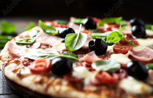 Pizza with ham, mozzarella cheese, cherry tomatoes, green and jalapeno pepper, black olives and fresh basil. Dark background. Close up. 