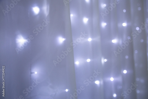 Luzes brancas acesas, desfocadas, em bokeh, com uma cortina de voal transparente por cima.