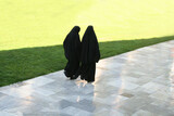 Two Arab women strolling in a garden on a sunny day..